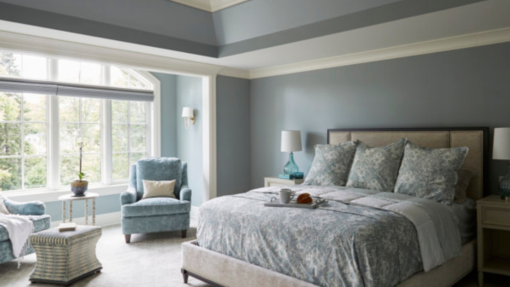 A tranquil blue and cream bedroom suite. There is a large master bed with a breakfast tray sitting on it and a large picture window and comfy armchair.