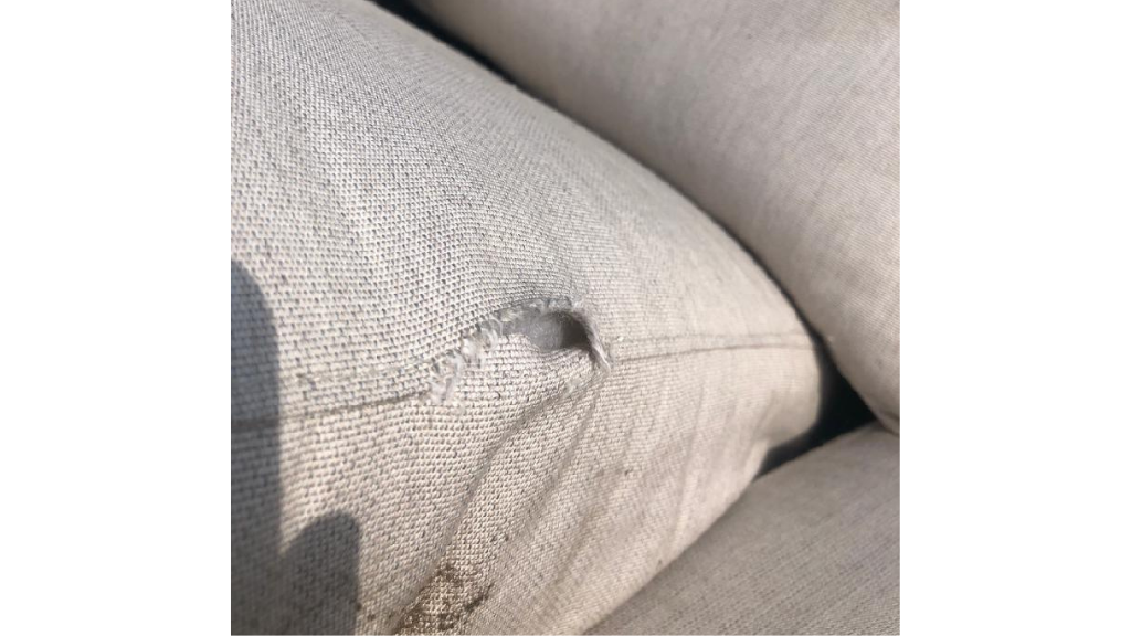 A gray couch with a large hole in the seam.