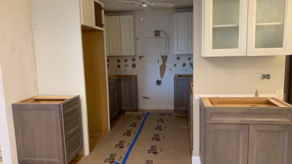 A kitchen is being prepared for demo day. There are two wood cabinets with the tops removed and painter's tape on the floor.