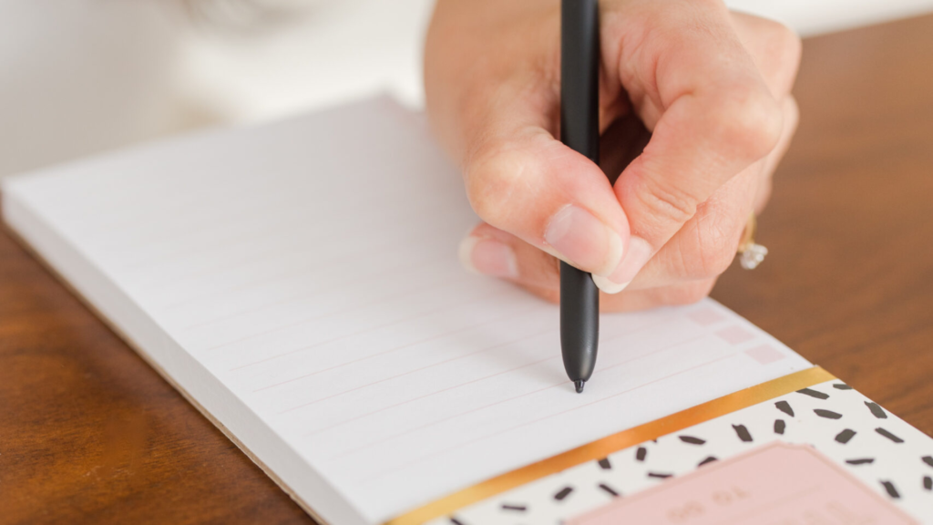 woman writes her word of the year on a pink notepad